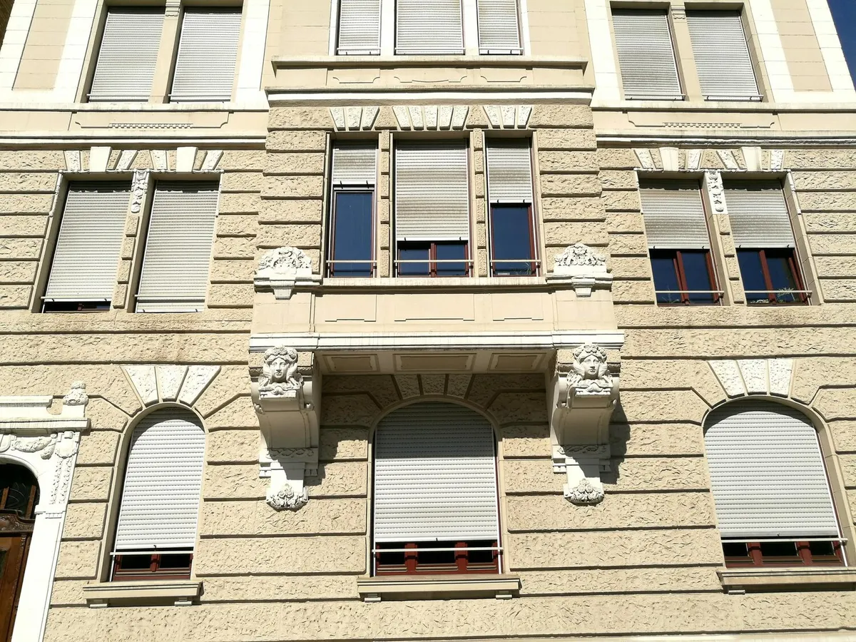 Façade d'immeuble ancien en pierre claire dont les fenêtres sont équipées de volets roulants à demi baissés