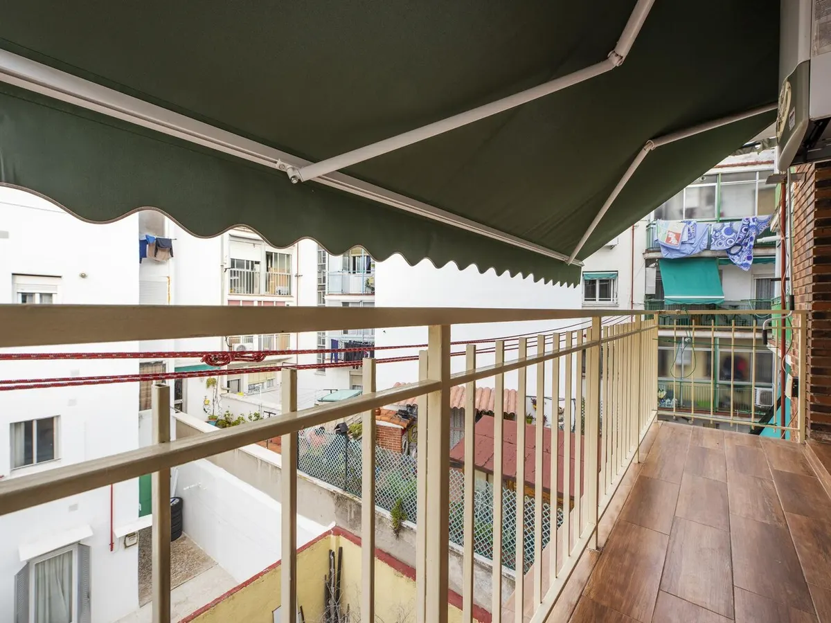 Store banne à bras articulés en toile verte déployé au-dessus d'un balcon d'appartement